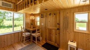 A wooden cabin interior with a dining area, a large window, and a dreamcatcher decoration. - Boho Beaver (Grey Highlands)