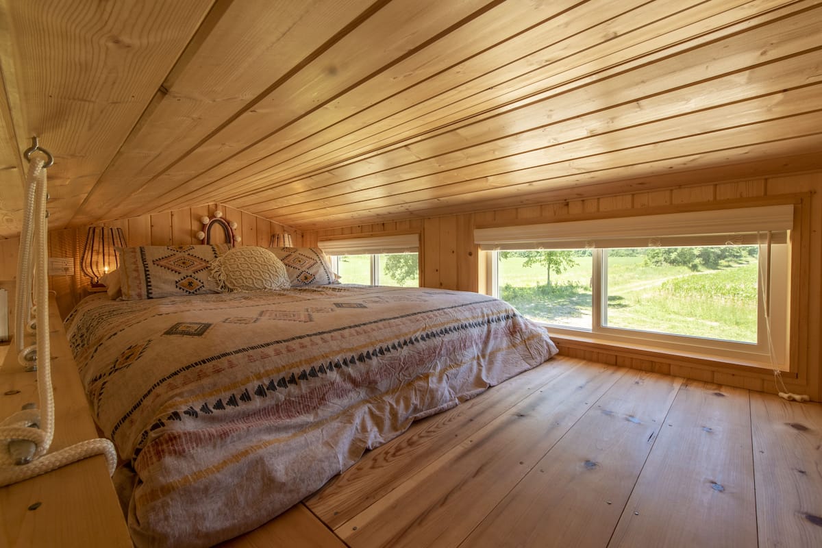 A wooden cabin bedroom with a large bed, two windows, and a wooden ceiling.