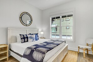 Een slaapkamer met een bed, nachtkastje, stoel, raam en spiegel.