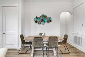 Een eetgedeelte met een houten tafel en rieten stoelen, een decoratief wandobject en een witte deur.