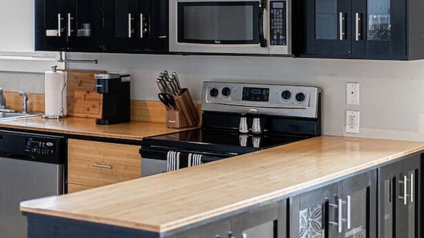 A modern kitchen with black cabinets, a microwave, a stove, and a wooden countertop.