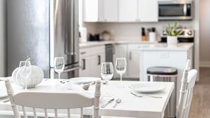 Une cuisine moderne avec des meubles blancs, un réfrigérateur en acier inoxydable et un coin repas avec une table blanche mise pour deux personnes.