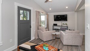 Un salon moderne doté d’un ventilateur de plafond, d’un téléviseur à écran plat et de deux fauteuils gris.