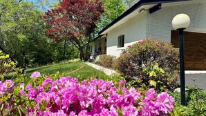 Una casa amb façana de maó, un porxo i un jardí amb flors roses.