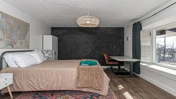 A bedroom with a bed, a desk, a chair, a map on the wall, and a window with a view of trees.