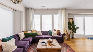 A living room with a purple sectional sofa, a wooden coffee table, and a large plant. - Family Beach Home ~Steps to Beach~Hot Tub~Game Room~Sleeps 13! (Surf City)