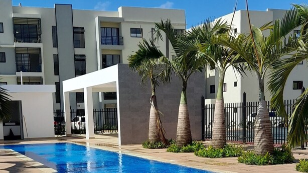 Una piscina con bordo piastrellato, circondata da palme e edifici moderni.