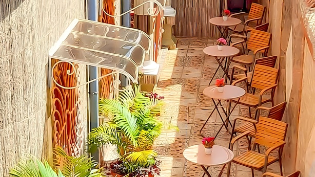 A sunlit outdoor seating area with multiple round tables and chairs, surrounded by potted plants and a decorative metal awning. - Farhyda & Frères Hôtels  (Bangangte)
