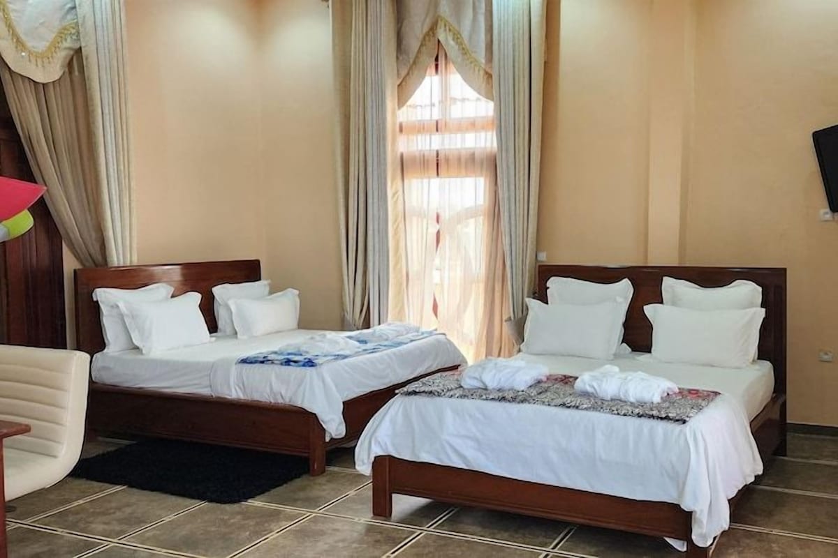 A hotel room with two single beds, a chair, a TV, and curtains.