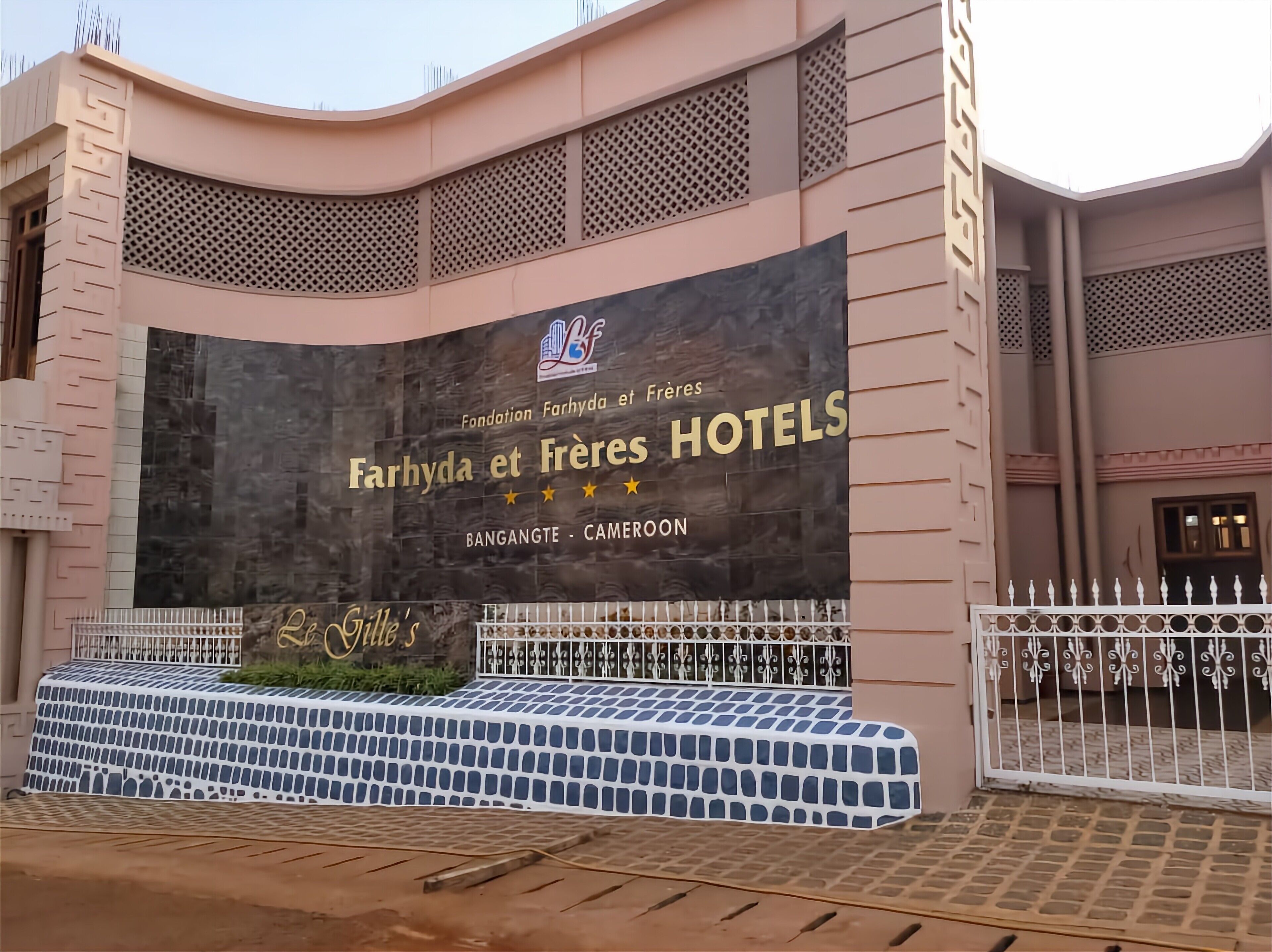 A hotel facade with a large sign for Farhya et Frères Hotels, a gated entrance, and a patterned awning.