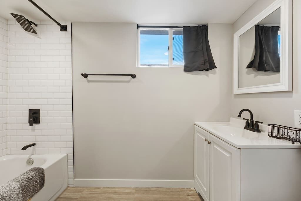 Une salle de bain avec une baignoire, une douche, une fenêtre avec des rideaux et un lavabo avec un miroir.