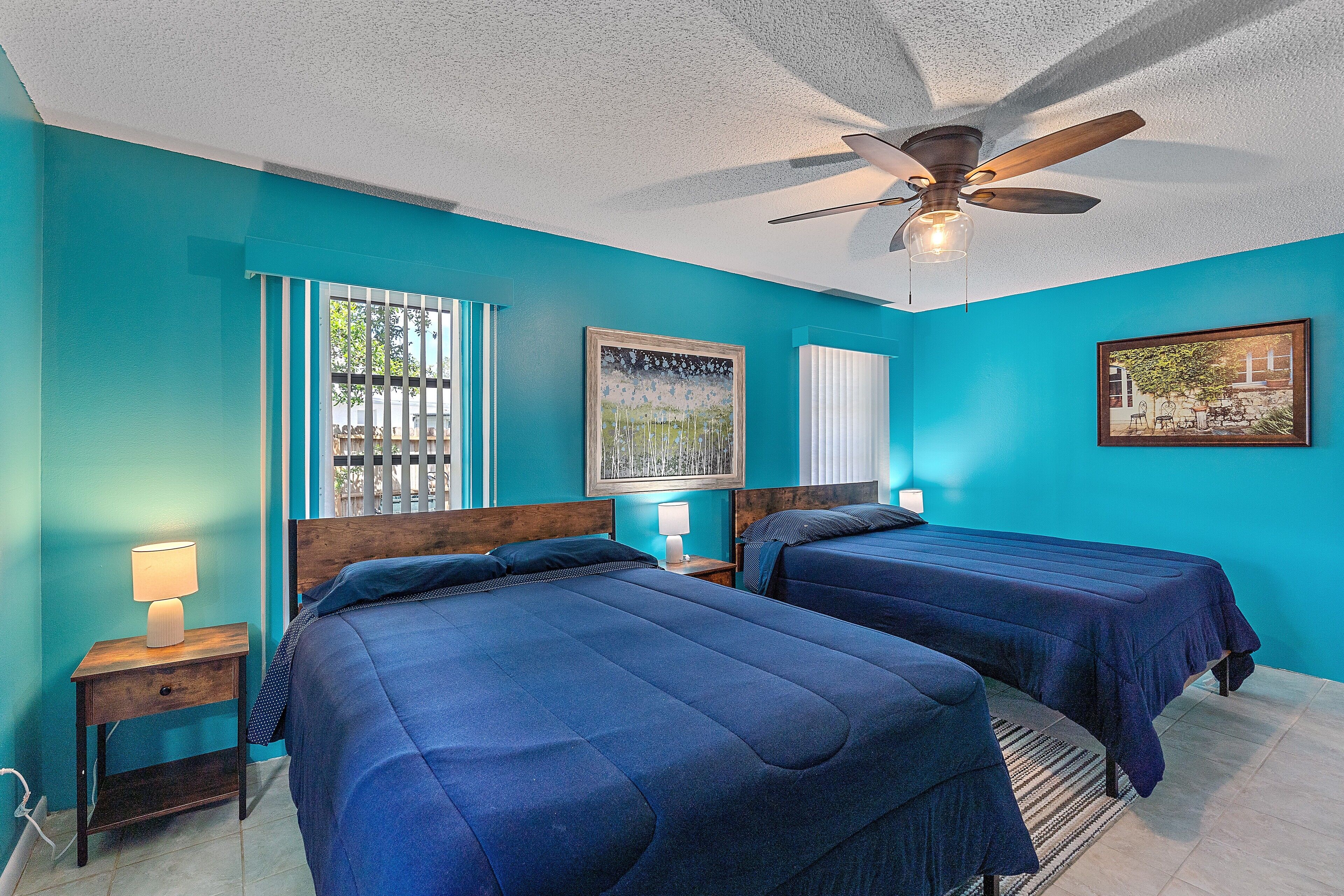 A room with two beds, a ceiling fan, and artwork on the walls.