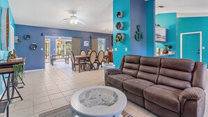 A spacious living room with a brown leather sofa, a glass coffee table, and a dining area with wooden furniture. - House with outdoor pool and jacuzzi with canal to the ocean, kayaks, bicycles (Port Charlotte)