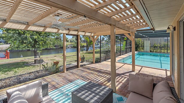 A covered patio with a pool, outdoor furniture, and a view of a swimming pool and greenery. - House with outdoor pool and jacuzzi with canal to the ocean, kayaks, bicycles (Port Charlotte)