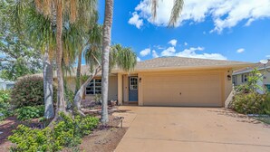 A residential house with a garage, palm trees, and a clear blue sky. - House with outdoor pool and jacuzzi with canal to the ocean, kayaks, bicycles (Port Charlotte)