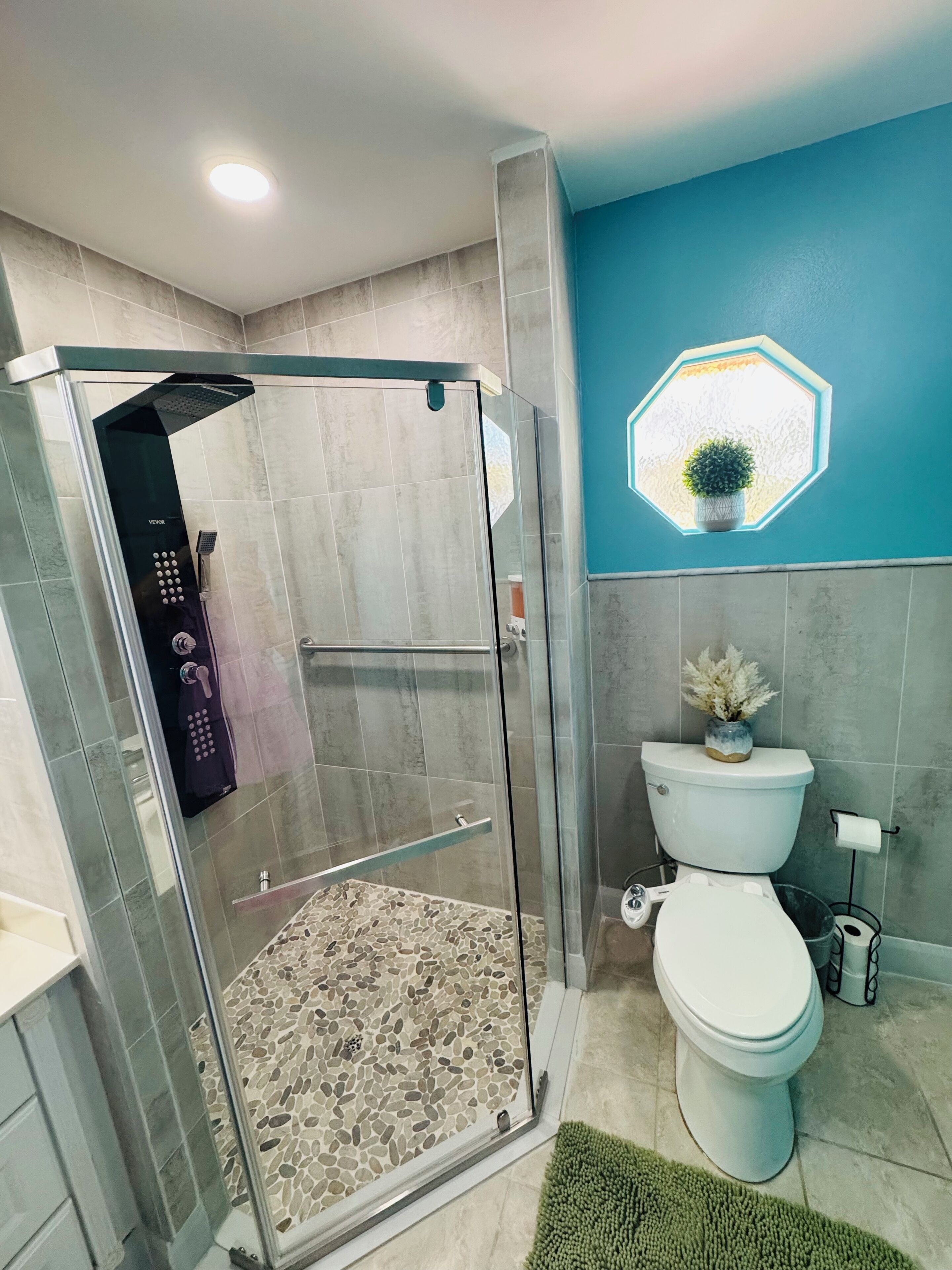 A modern bathroom with a glass-enclosed shower, a toilet, and a decorative hexagonal window.