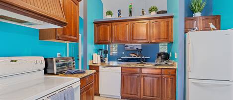 Une cuisine avec des meubles de rangement en bois, un réfrigérateur blanc, un lave-vaisselle, une cuisinière et un ventilateur de plafond.