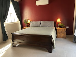 Une chambre à coucher comprenant un lit, deux tables de chevet avec des lampes, une fenêtre avec des rideaux et un climatiseur fixé au mur.