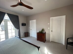 A bedroom with a bed, a ceiling fan, a dresser, and two doors.