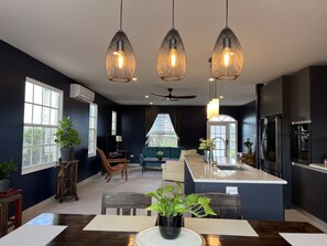 A modern kitchen with a central island, dark walls, and pendant lighting.