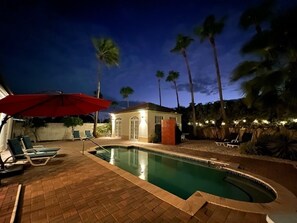 A swimming pool area with lounge chairs and an umbrella.