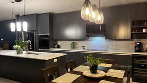 Una cocina moderna con armarios oscuros, una isla central con un lavamanos y un comedor con una mesa y sillas de madera.