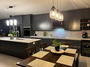 A modern kitchen with dark cabinetry, a central island with a sink, and a dining area with a wooden table and chairs.