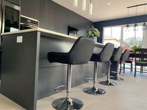 A modern kitchen with a dark grey island, stainless steel appliances, and black bar stools.
