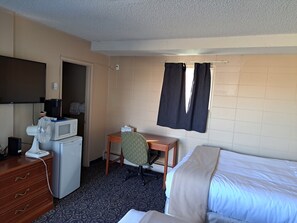 A hotel room with a bed, a desk with a chair, a microwave, a fan, and a television. - Matador Motel (Drayton Valley)
