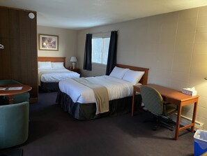 A hotel room with two beds, a desk, a chair, a small table, a clock, a picture, and a window with curtains. - Matador Motel (Drayton Valley)