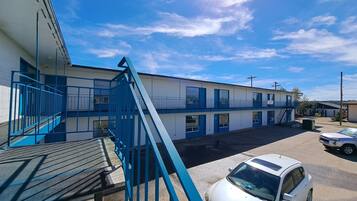 A motel with a blue staircase leading to a balcony, a parking area with a white car, and a clear blue sky.