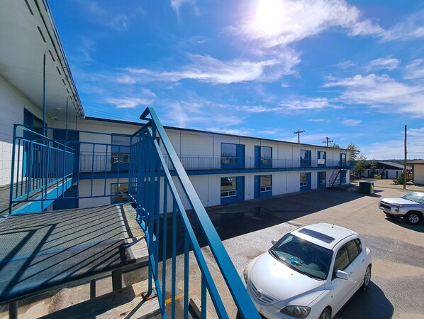 A motel with a blue staircase leading to a balcony, a parking area with a white car, and a clear blue sky. - Matador Motel (Drayton Valley)