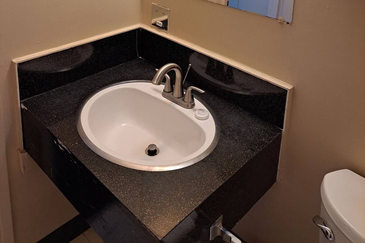 A bathroom with a white sink, black countertop, and a mirror above it. There is a towel rack with towels on the wall.