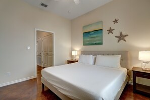 A bedroom with a large bed, a nightstand with a lamp, a door leading to another room, and a wall with a painting and star decorations.