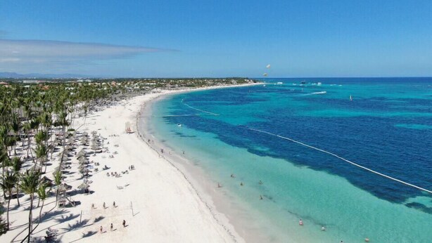 A beach with clear turquoise waters, a sandy shore lined with palm trees, and a few people enjoying the beach. - Blue Garden Apartment Los Corales (Punta Cana)