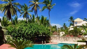 A clear blue pool surrounded by palm trees and a stone pathway. - Blue Garden Apartment Los Corales (Punta Cana)