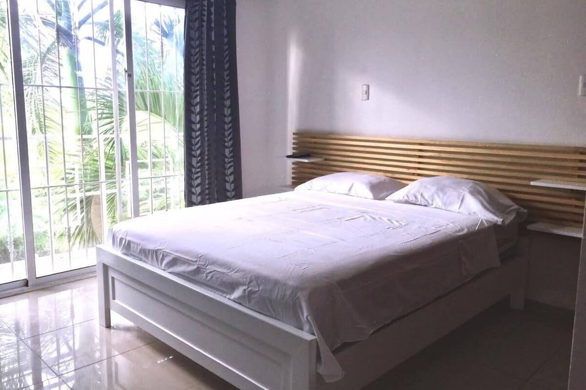 Un dormitorio con cama, mesita de noche y vista a palmeras a través de un gran ventanal.