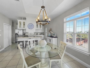A modern kitchen with white cabinets, a central island, and a dining area with a glass table and white chairs.