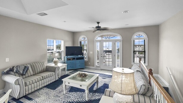 A spacious living room with a sofa, coffee table, and TV, featuring large windows and a staircase. - Paradise By The Pier 2 Bedroom Home by RedAwning (Panama City Beach)