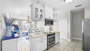 A modern kitchen with white cabinetry, a built-in microwave, a stainless steel refrigerator, and a central island with a stove. - Paradise By The Pier 2 Bedroom Home by RedAwning (Panama City Beach)