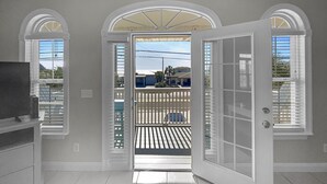A room with a large open door leading to a balcony with a view of the street and buildings. - Paradise By The Pier 2 Bedroom Home by RedAwning (Panama City Beach)