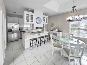 A modern kitchen with a central island, white cabinetry, and a large clock.
