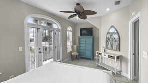 A bedroom with a large bed, a ceiling fan, a vanity with a mirror, and a blue cabinet. - Paradise By The Pier 2 Bedroom Home by RedAwning (Panama City Beach)