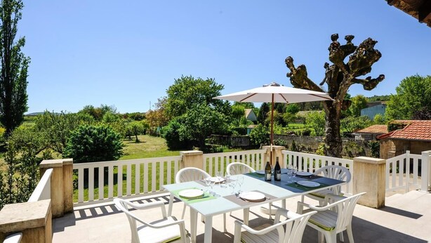 An outdoor patio with a table set for dining, surrounded by white chairs and a large umbrella. - Le Vivier - GIVRY - Gîte (GIVRY)