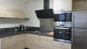 A modern kitchen with light wood cabinets, stainless steel appliances, and a black range hood. - Le Vivier - GIVRY - Gîte (GIVRY)