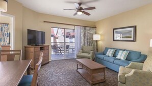 Ein Hotelzimmer mit Essbereich, einer Couch, einem Fernseher, einem Deckenventilator und einem Balkon mit Gartenmöbeln.