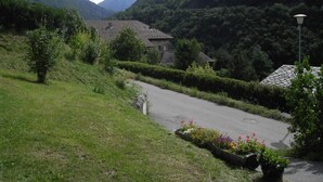 A rural road with a house on a hillside, surrounded by lush greenery and mountains.