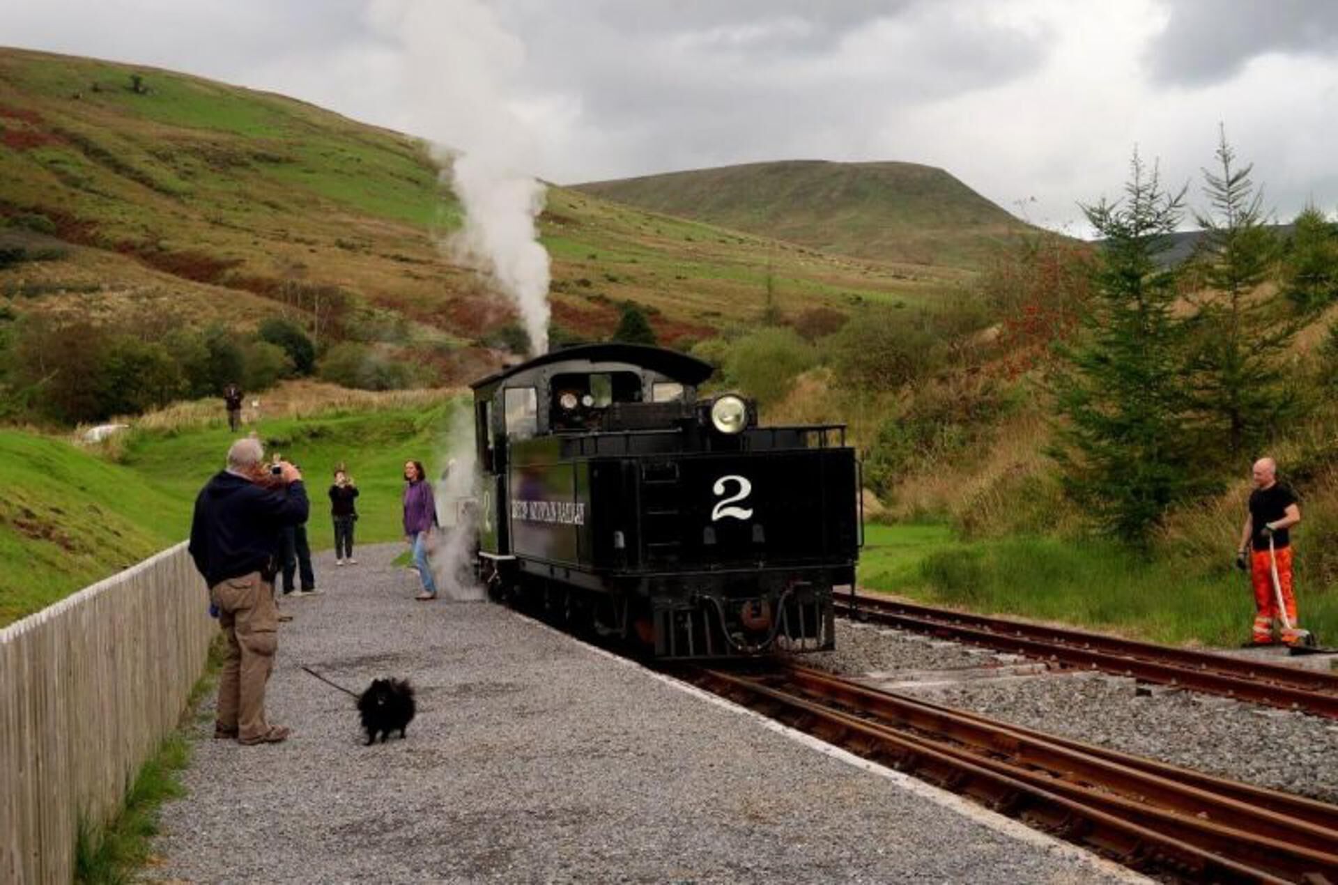 A steam locomotive numbered 2 on a railway track with people and a dog nearby.