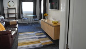 A modern living room with a leather sofa, a coffee table, a TV, and a dining area with a chair and a small table. - Gorgeous, Comfortable Apartment on the High Street (Merthyr Tydfil)