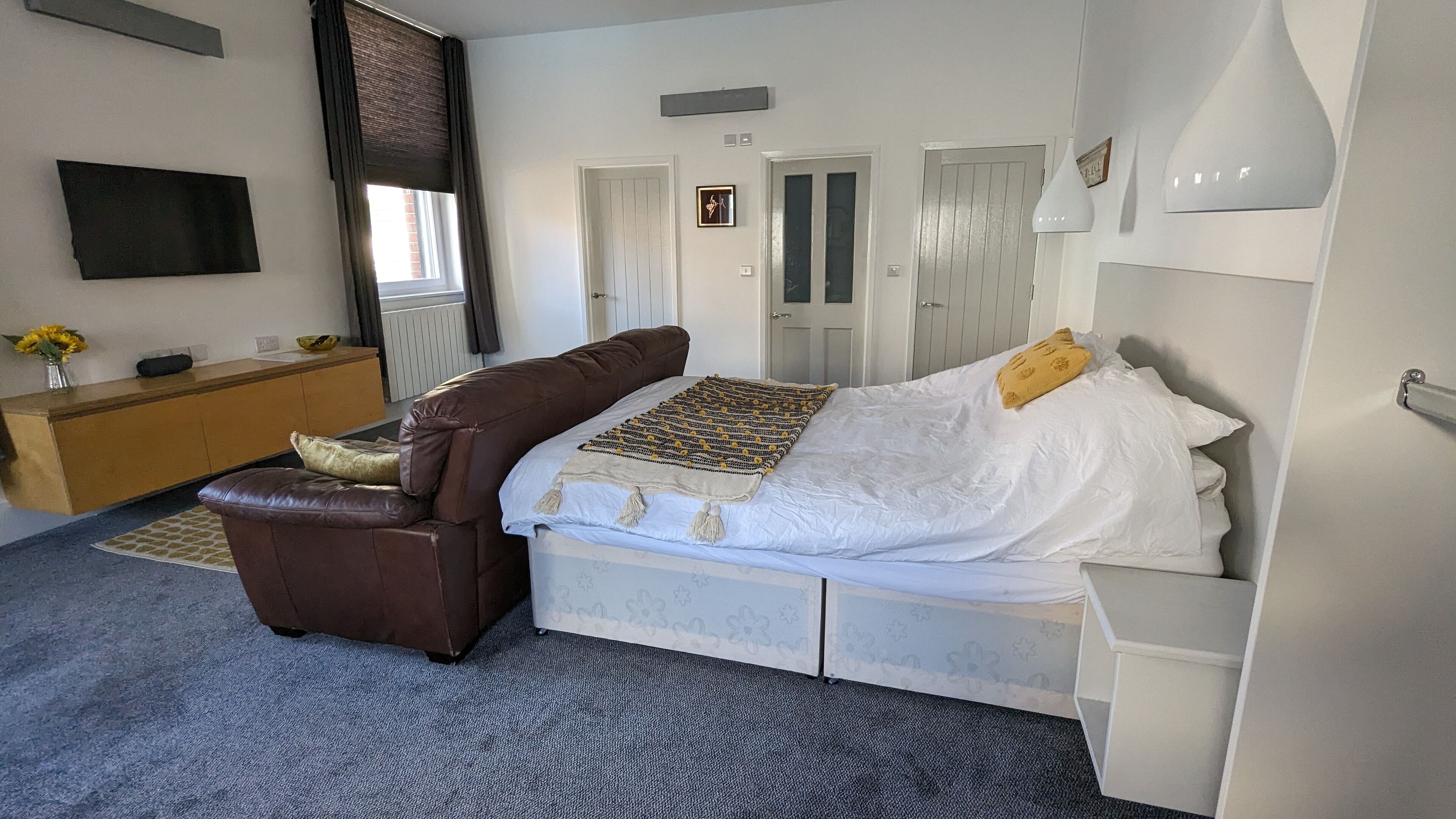 A bedroom with a bed, a brown leather chair, a wooden dresser, and a window with curtains.